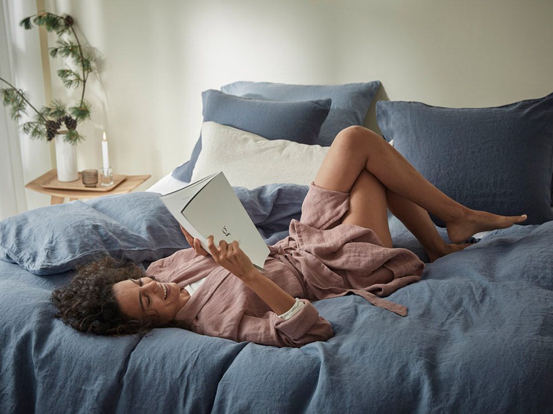Vrouw ligt te lezen op een bed met gewassen linnen in earth blue